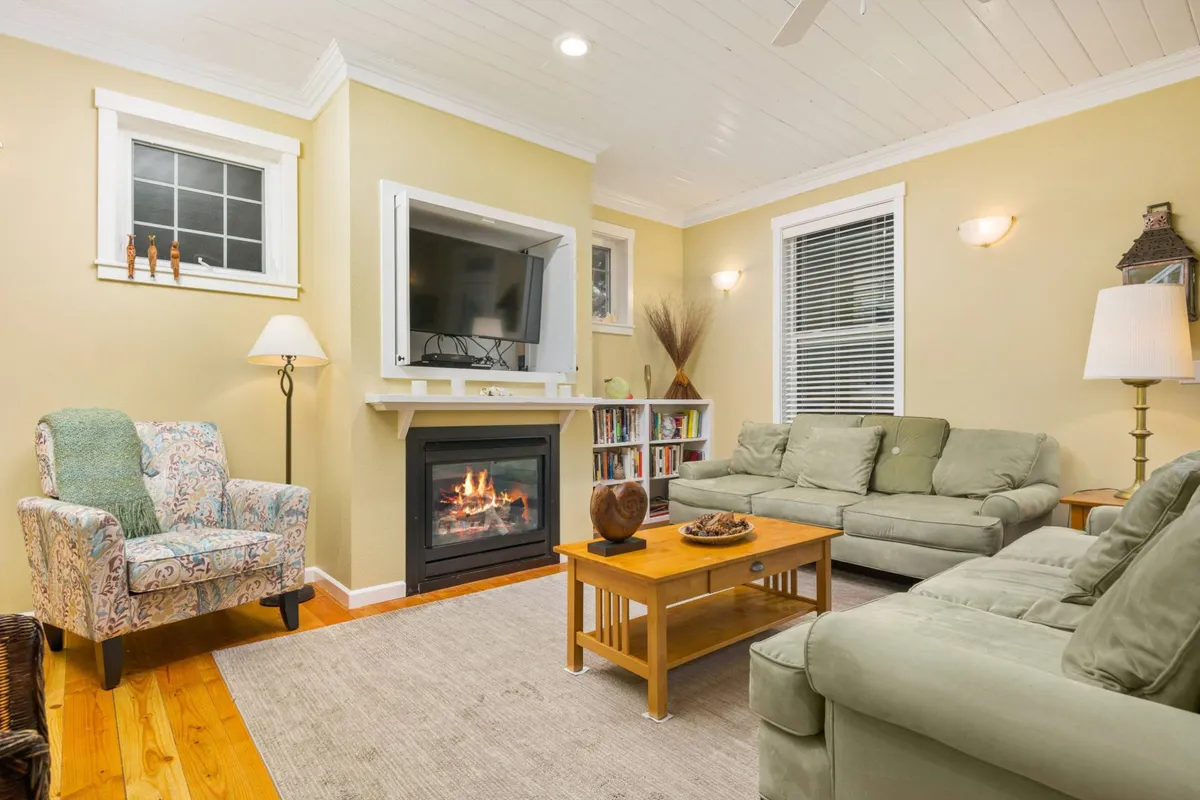 A warmly lit lounge area features a glowing fireplace, comfortable seating including a sofa and an armchair, and a well-stocked bookshelf. The scene suggests moments spent reading, sharing stories, or simply enjoying the ambiance together.