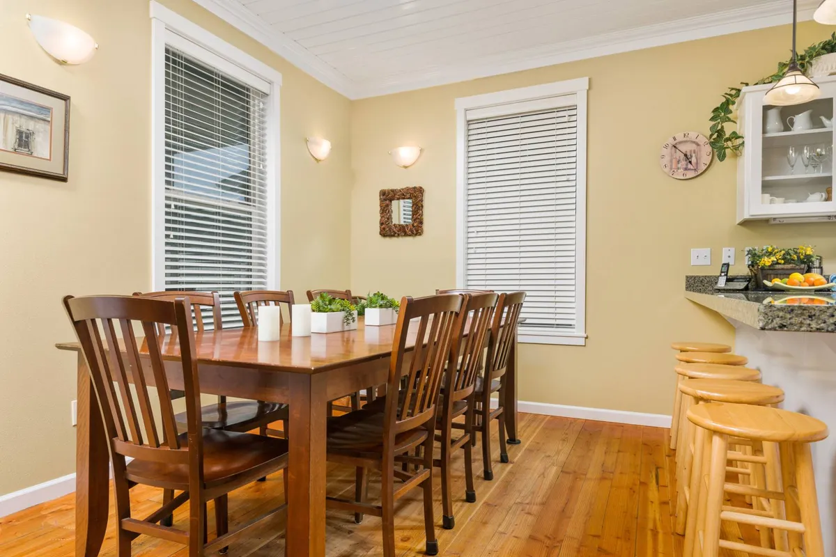 The dining area features a table with wooden chairs, a counter with bar stools, and decorative wall mirrors, offering an inviting space for shared meals and conversations. The view hints at a welcoming communal atmosphere.