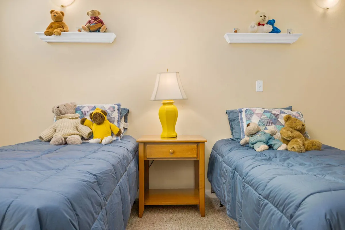A playful bedroom with two twin beds, a yellow lamp, and shelves filled with stuffed animals. This cheerful setting is clearly appealing for families with children and hints at the comfort and safety of a home where kids can rest after exploring community amenities like the playground.